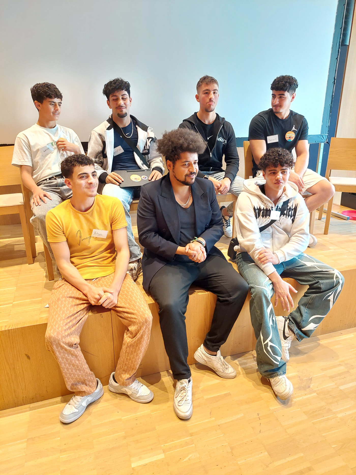 Podiumsdiskussion auf dem Fachtag. Sieben Personen sitzen zufrieden an und auf einer Bühne und blicken gemeinsam zu einem Punkt im Raum.