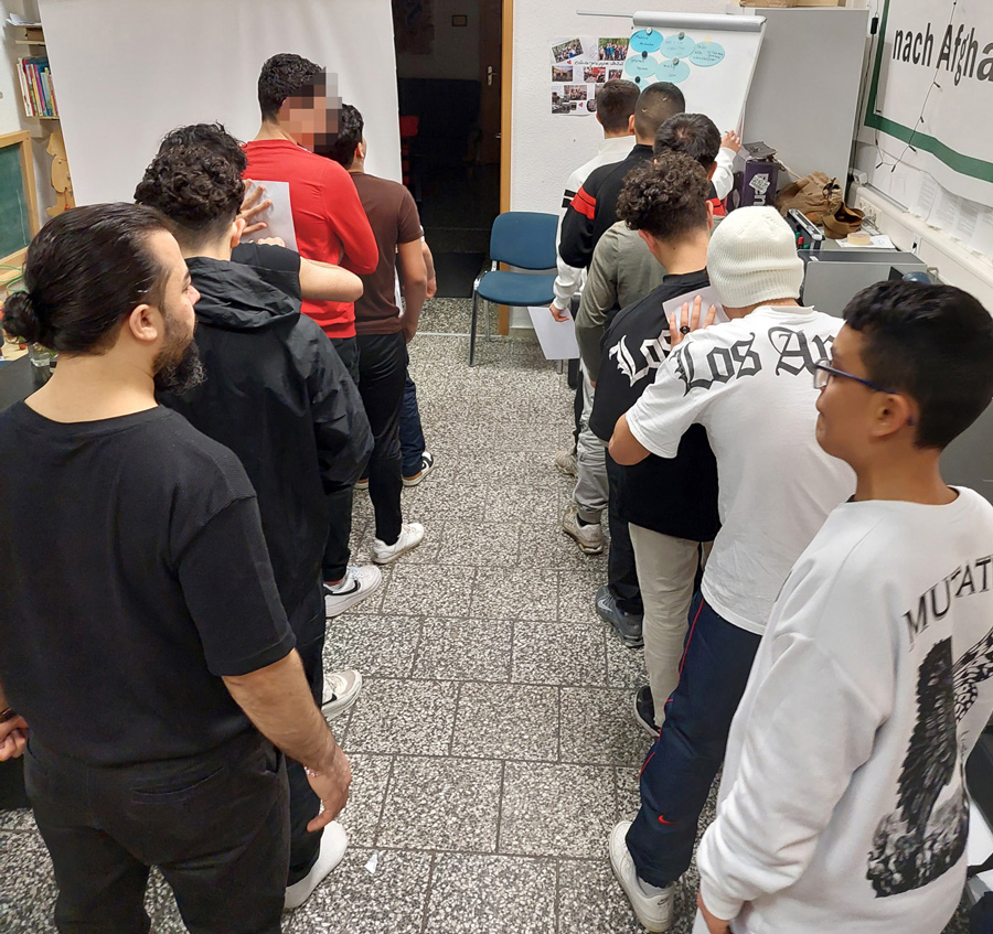 Workshop-Methode: Warmer Rücken. Jungen stehen in zwei Reihen und notieren etwas auf einem Blatt Papier, jeweils auf dem Rücken des Vorausstehenden