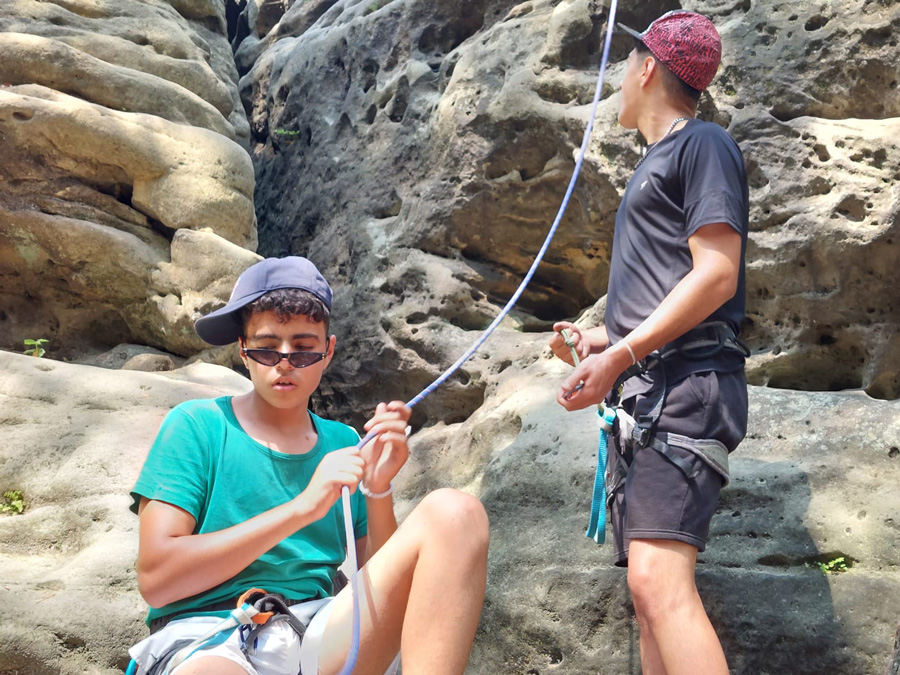 Zwei Jungen sichern eine Kletter-Leine am Fuße einer Steinwand